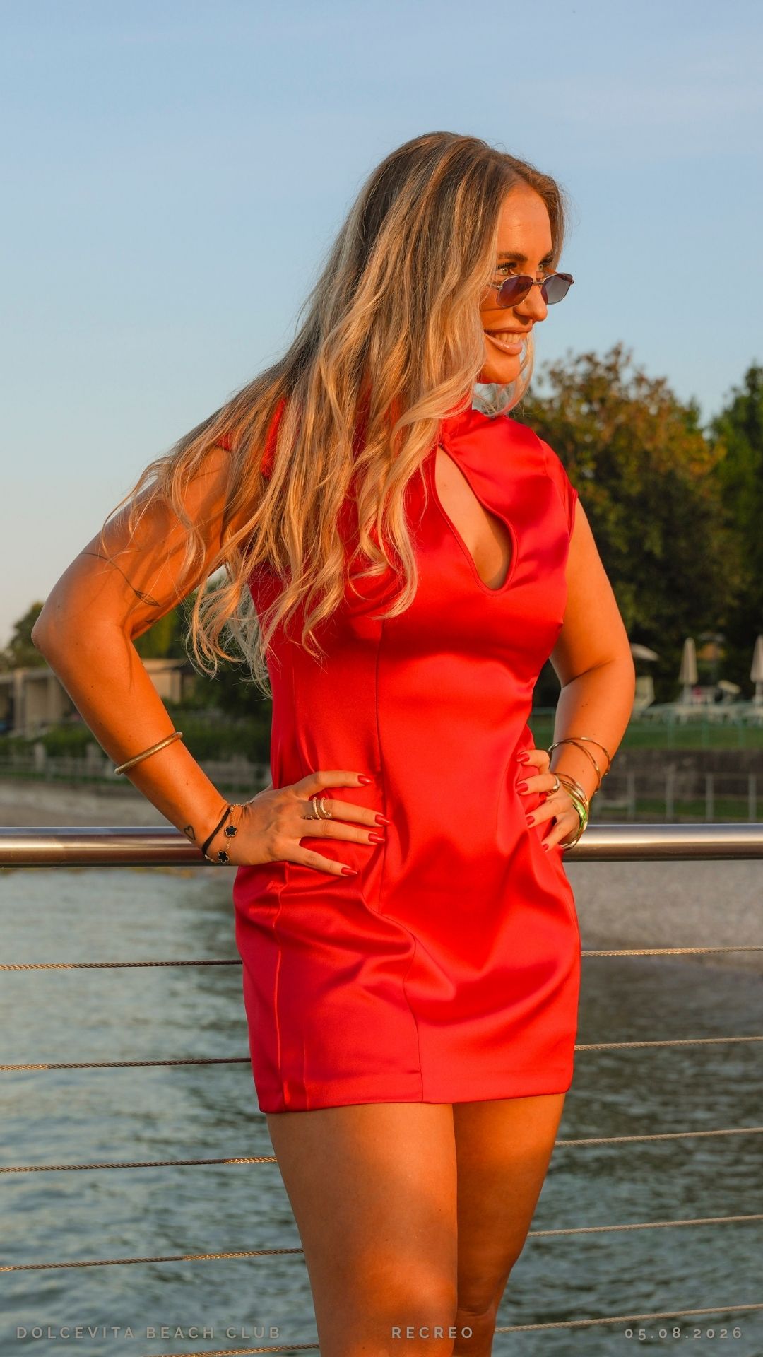 Ospite in abito rosso posa sul pontile al tramonto