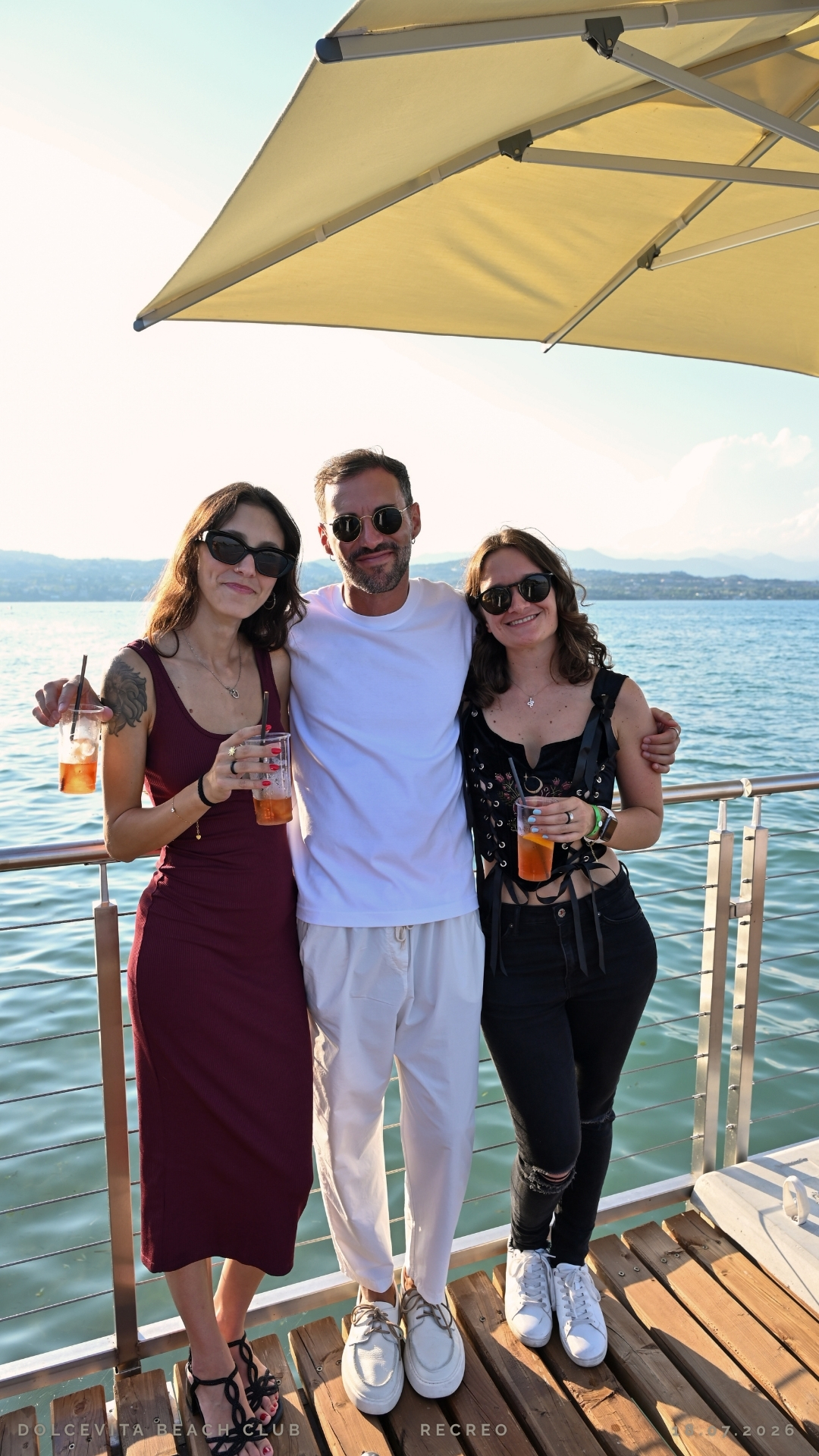 Tre amici posano insieme con drink vista lago