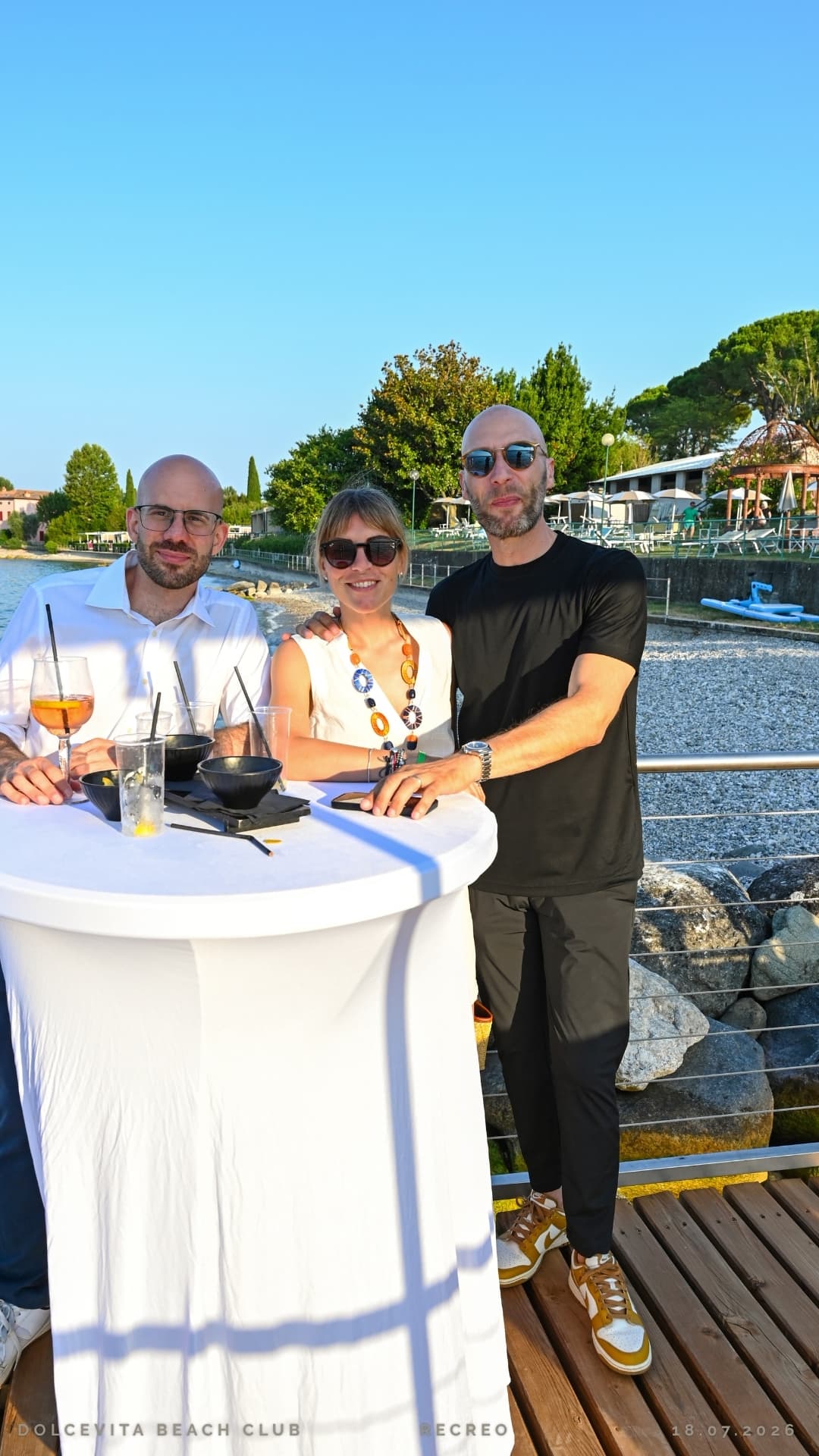 Tre ospiti posano al tavolo alto con vista sulla spiaggia