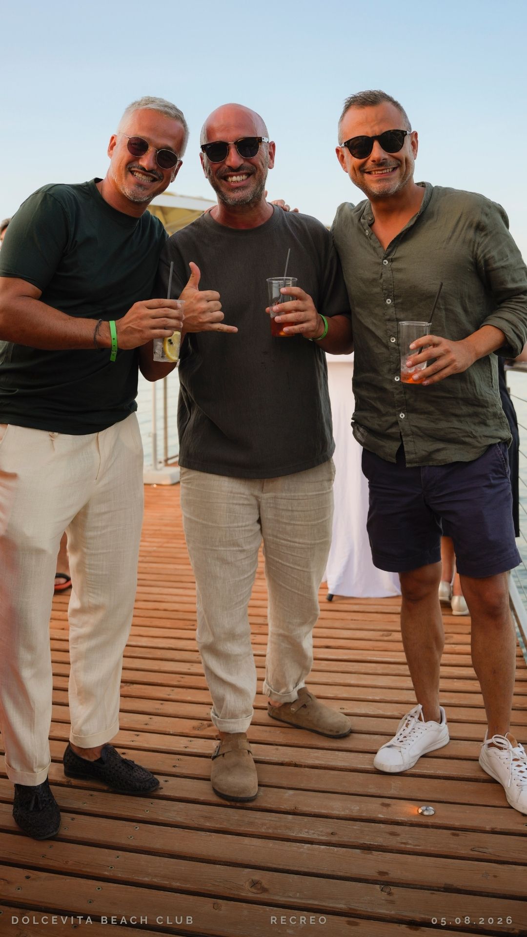Tre amici brindano con drink sul pontile