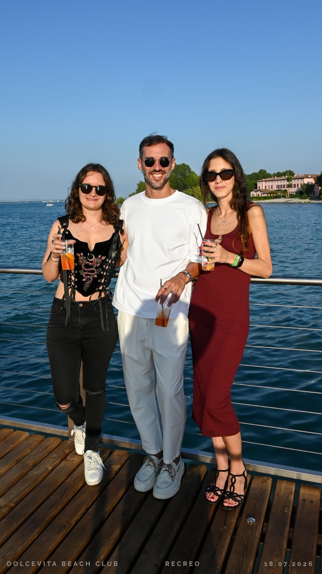 Tre ospiti posano con i cocktail sul pontile vista lago