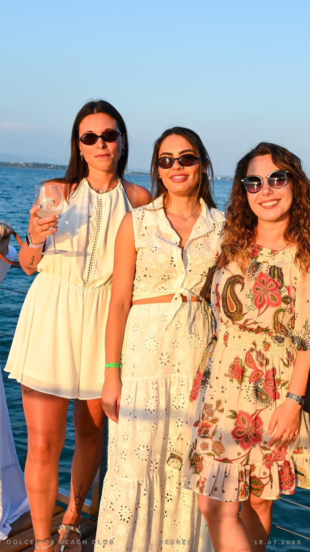 Tre amiche in abiti chiari brindano al tramonto